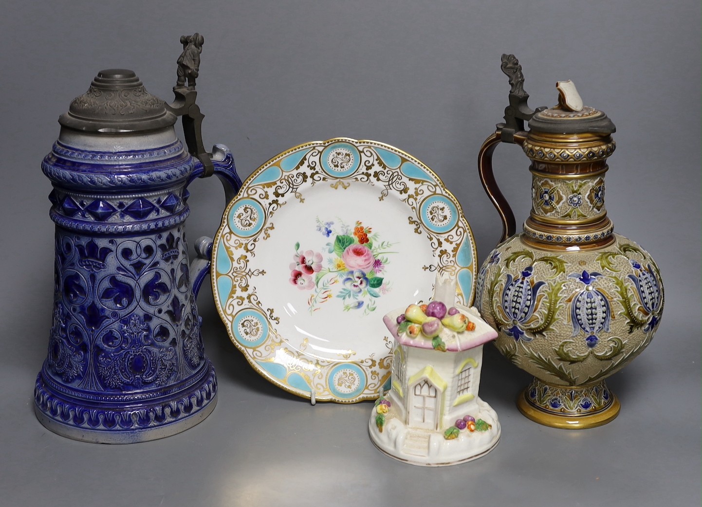 A Mettlach stoneware stein, 29.5 cm high, a German blue stoneware stein, a Staffordshire porcelain cottage pastille burner and an English porcelain floral plate